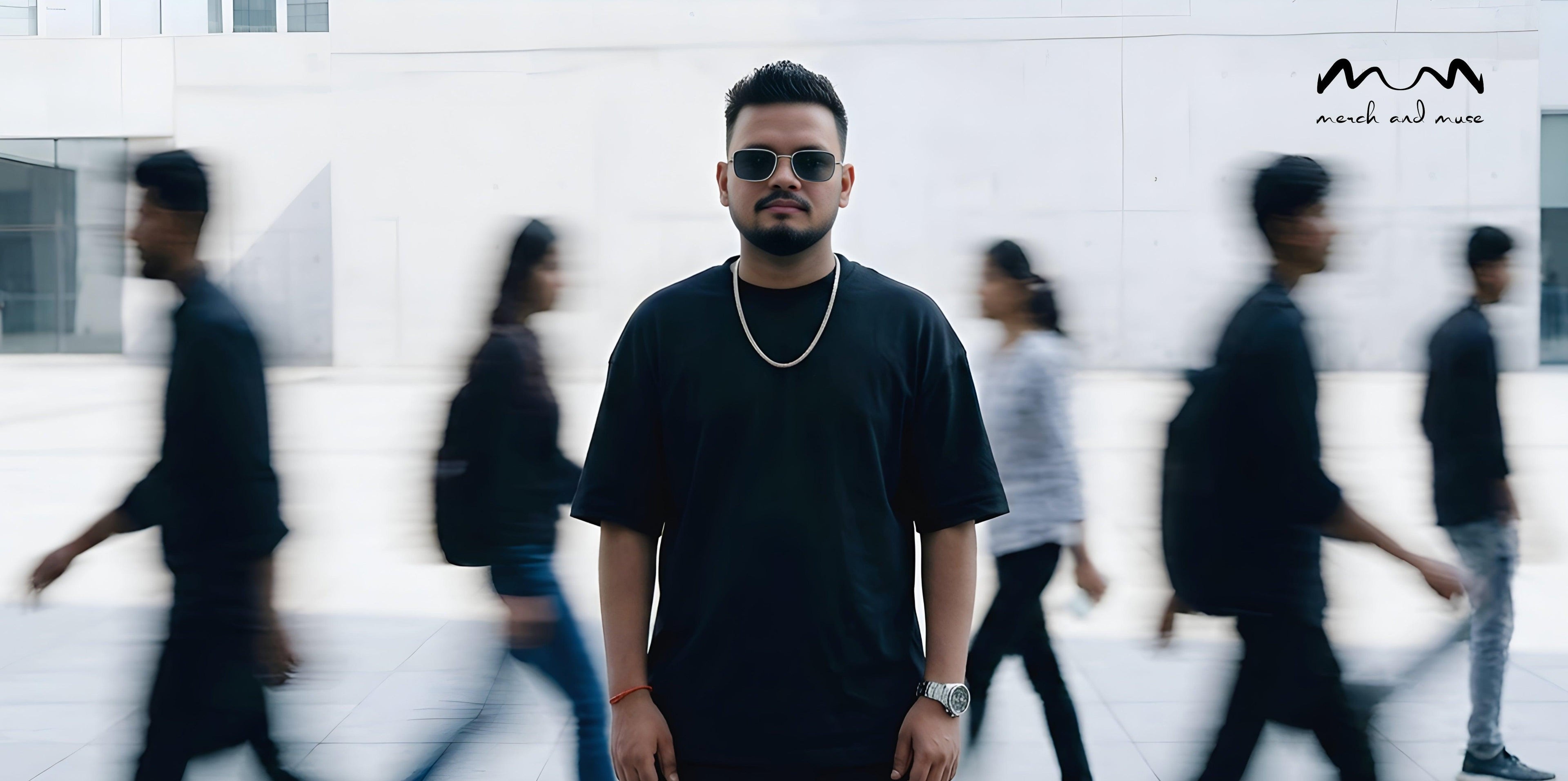 Man in black outfit standing in front of a blurred crowd with 'MERCH AND MUSE' logo.